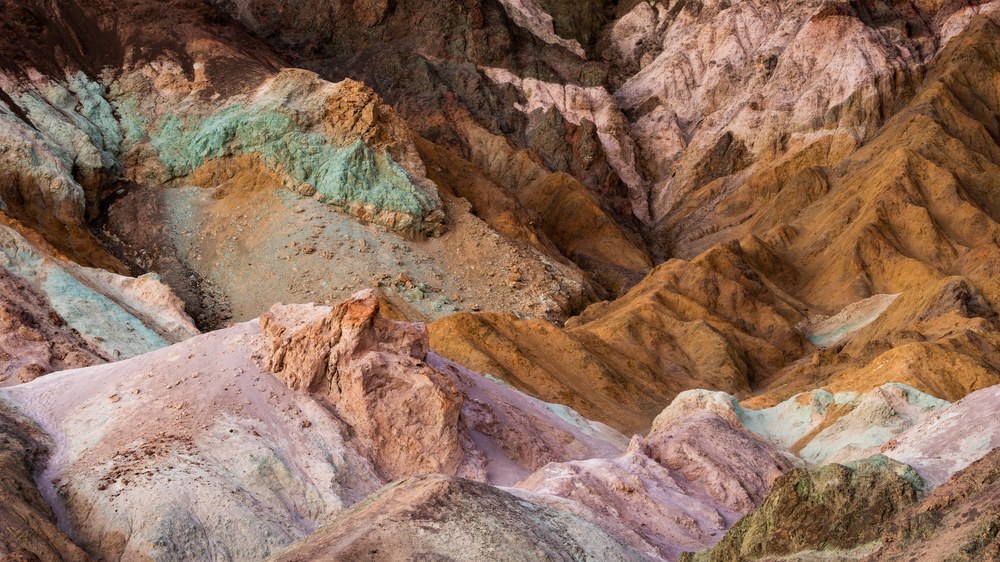 Eroded badland hills carry mineral colour in bands — turquoise, pink, rust and tan — with no sky in the frame.
