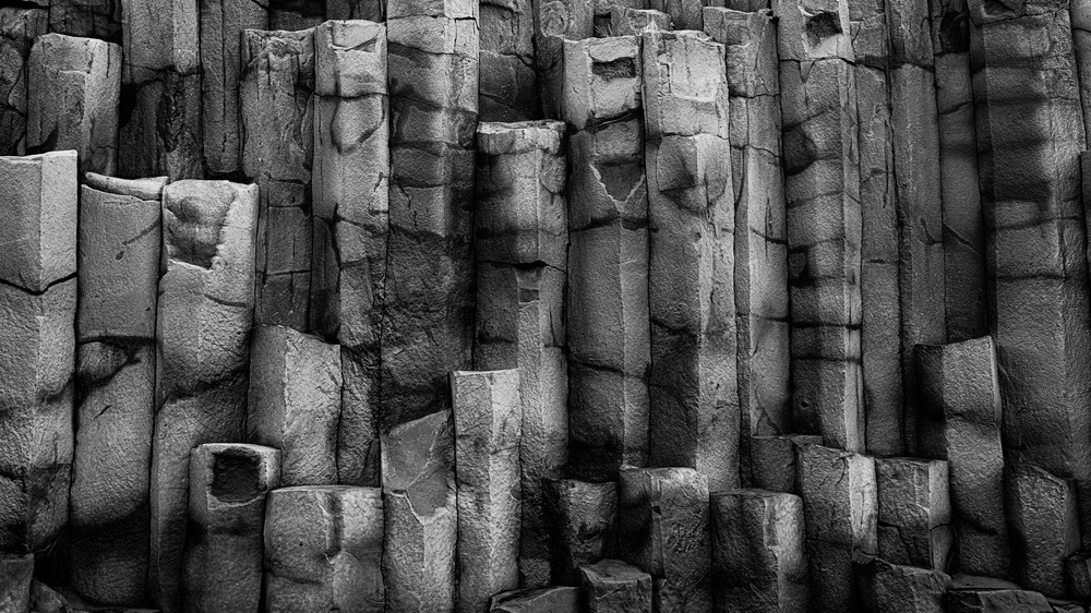 A black and white study of fractured basalt columns packed edge to edge, their tops broken off at different heights.