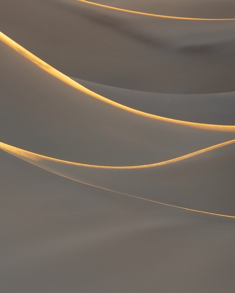 Three thin crest lines catch gold light across soft grey dune slopes, everything else in flat shade.