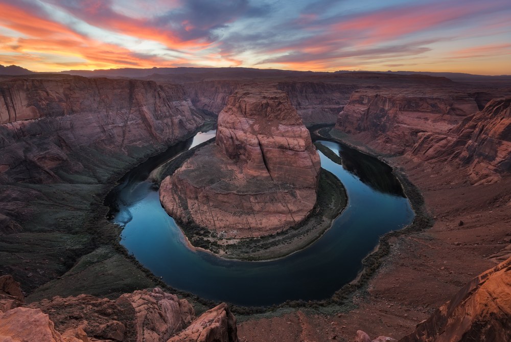 A river loops in a tight horseshoe around a flat-topped butte far below the canyon rim at sunset.