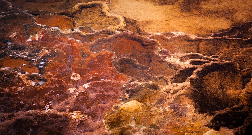 A close view of hot spring terraces where rust, orange and white mineral crusts run into one another in lobes.