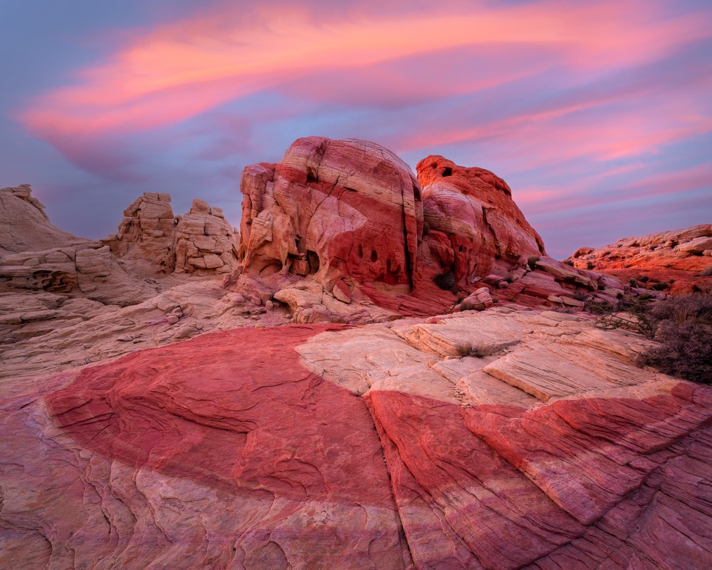 Banded red and white sandstone swells and domes under a pink and violet dusk sky, the nearest slab striped like grain.