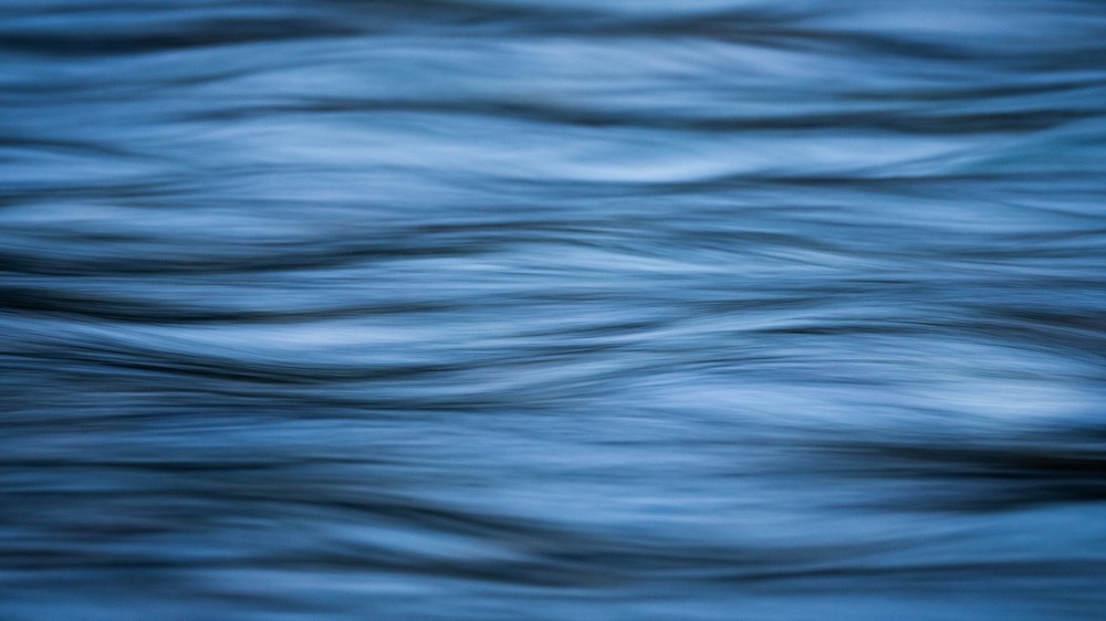 A close, soft-focus study of blue water in low undulating ripples, with no horizon or shore in the frame.