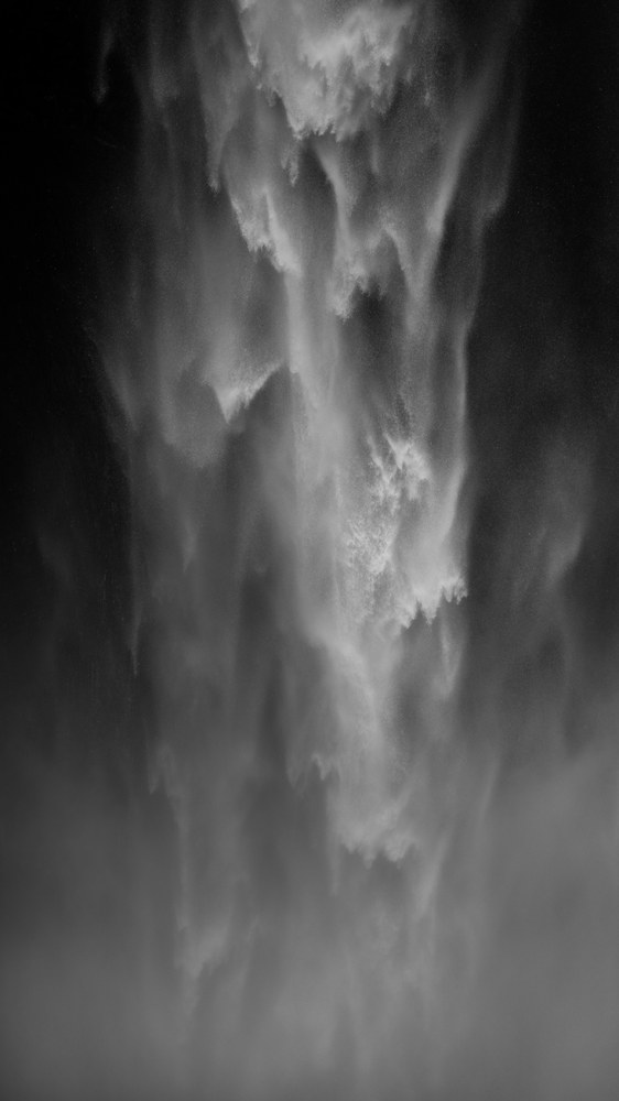 A close abstract of falling water — pale plumes and spray texture on near black, with no landscape visible.